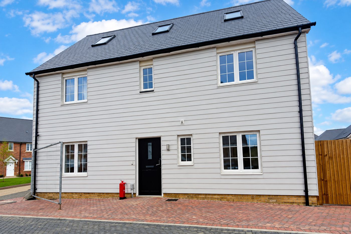 A detached house with pale cladding and a black front door